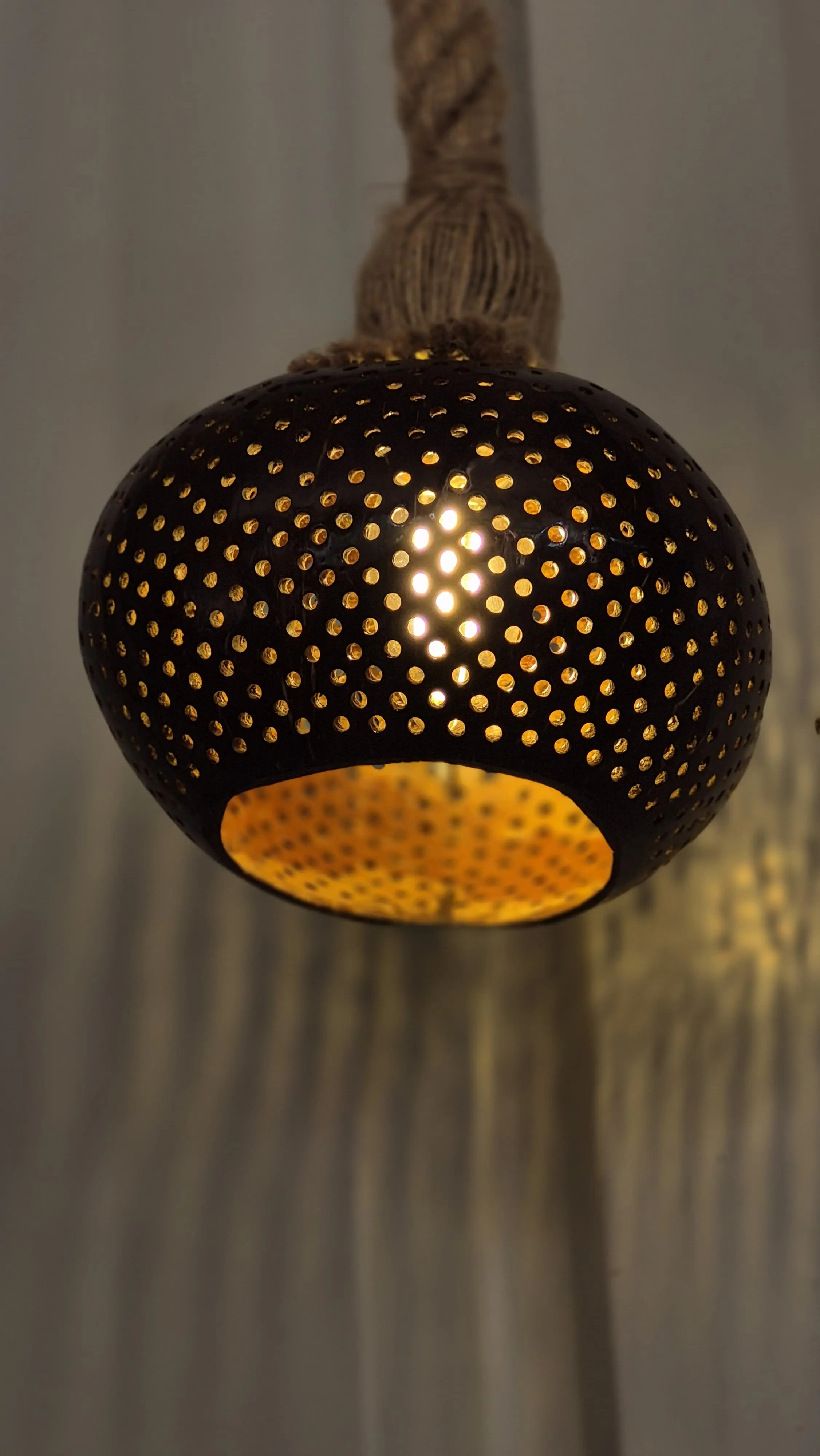 Coconut shell hanging lamp casting warm patterned light in a Guhagar workshop